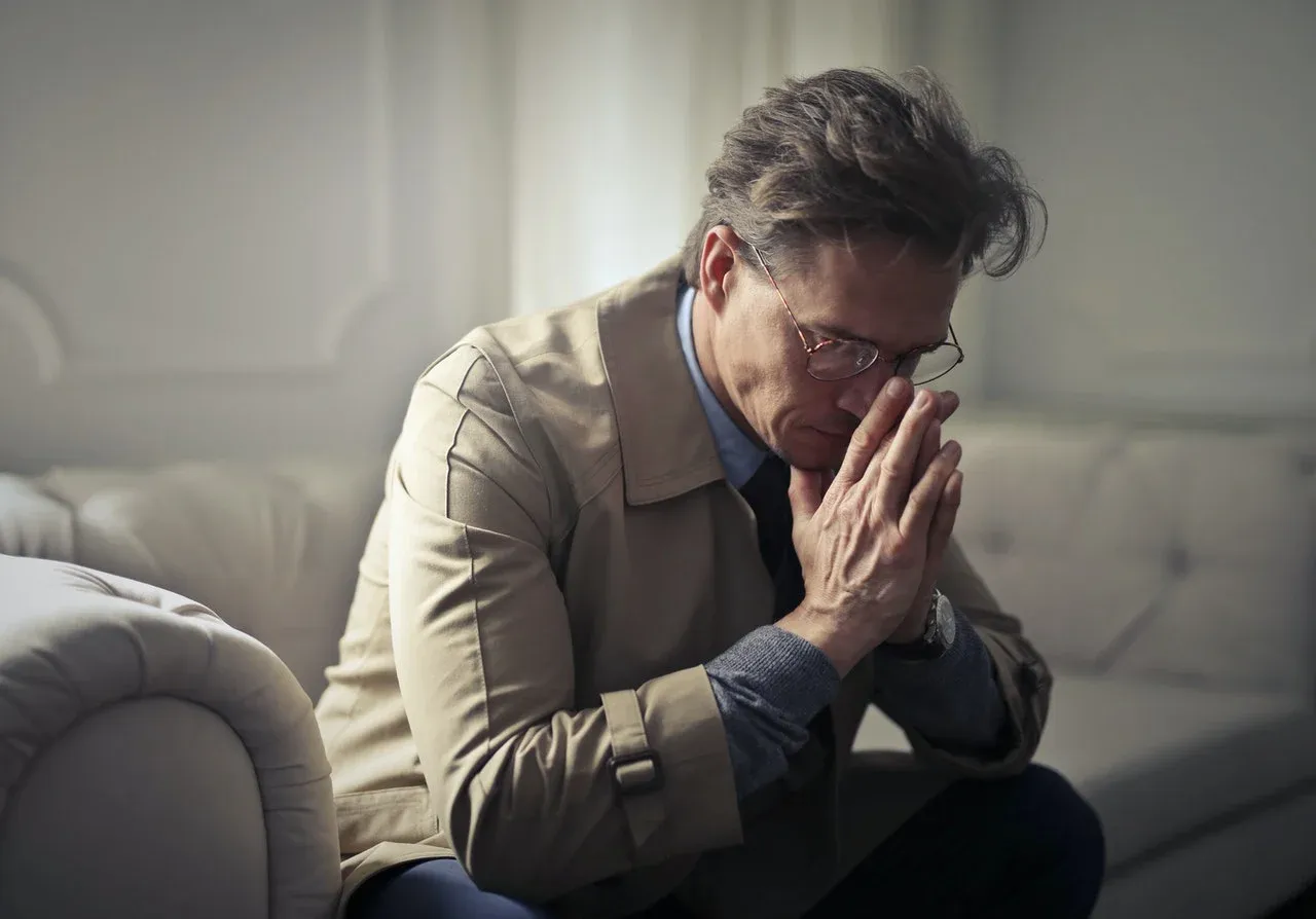 a man looking down while resting his chin on his folded hands